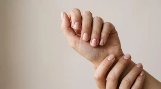 Manos femeninas mostrando uñas decoradas con diseños minimalistas de puntos elegantes creados con punzón