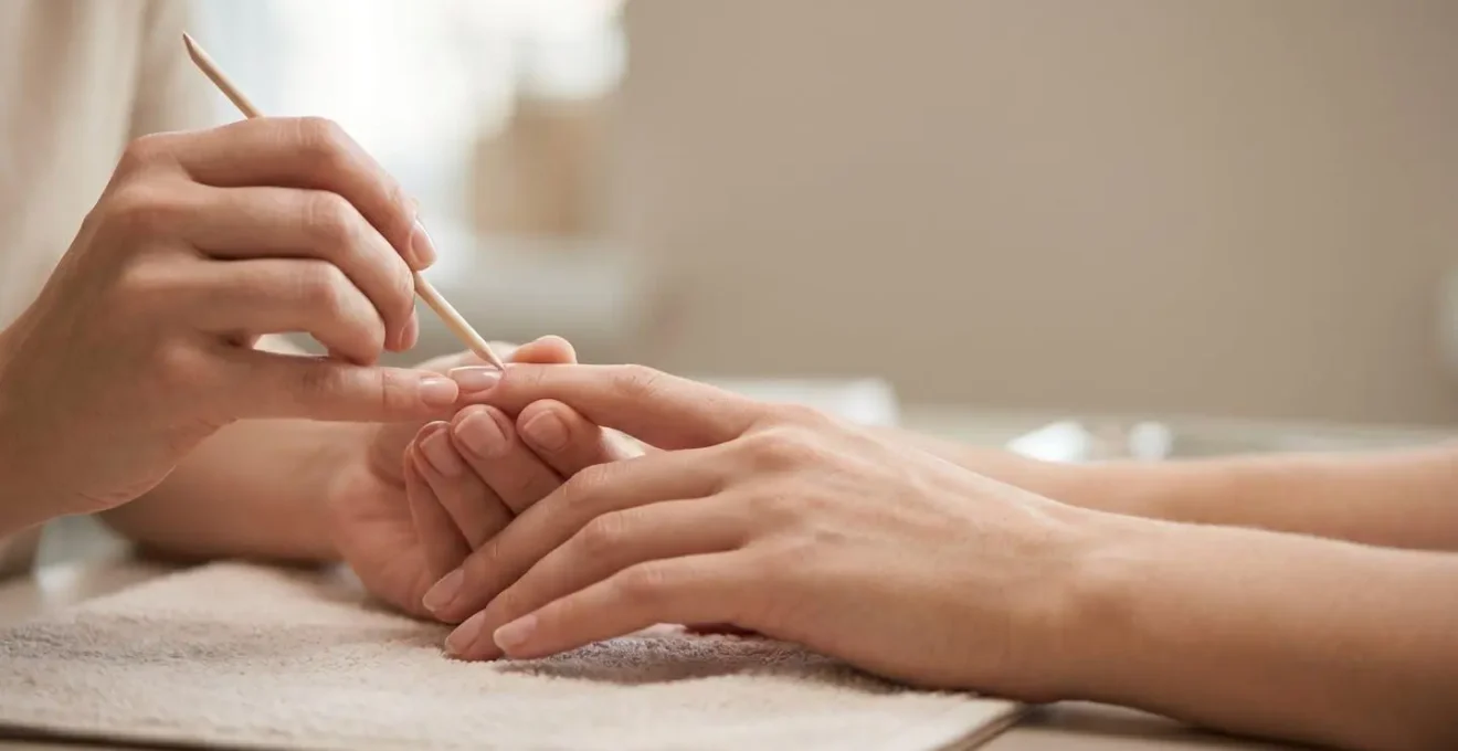 Primer plano de manos con cutículas perfectamente cuidadas recibiendo tratamiento profesional de manicura en ambiente natural