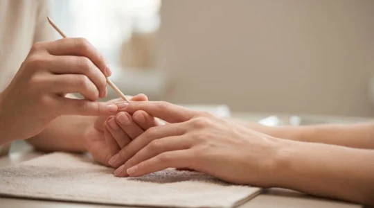 Primer plano de manos con cutículas perfectamente cuidadas recibiendo tratamiento profesional de manicura en ambiente natural